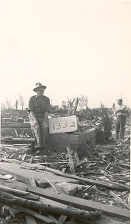 Man in front of destroyed home and address sign. 