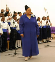 Choir director in blue dress standing in front of group.