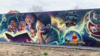image of the mural on the east side of the Library designed and painted by nationally recognized Flint artist Kevin Burdick; imagery shows families reading books and book characters like winnie the pooh 