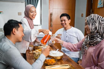 Four people, two men and two Muslim women wearing Hijba, sit around a table filled with food and nonalcoholic beverages.
