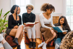 Four young women of color sit together, each pair sharing a different book to look at.