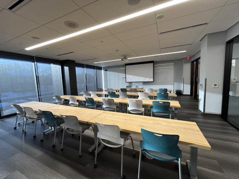 Photo of meeting room with four rows of tables and chairs classroom style and ceiling mounted projector screen.