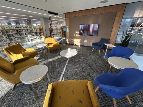 Photo of room with seven lounge chairs, several coffee tables and monitor on wall.