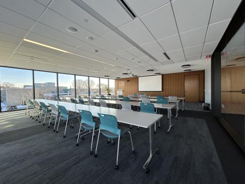 Photo of large room with tables and chairs classroom style and ceiling mounted screen.