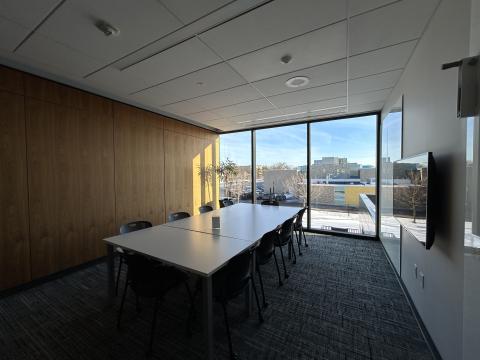 Photo of meeting room with table, ten chairs, large monitor on wall and white boards.