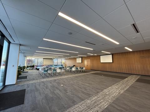 Photo of large meeting room with stage, forty chairs theater style, and three ceiling mounted projector screens.
