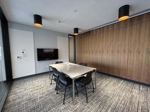 Photo of meeting room with table, six chairs, large monitor on wall and pin boards.