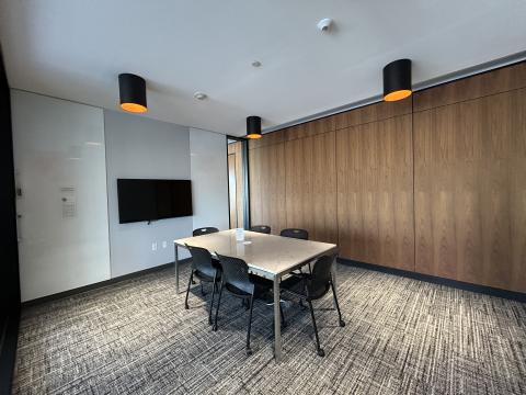 Photo of meeting room with table, six chairs, large monitor on wall and white boards.
