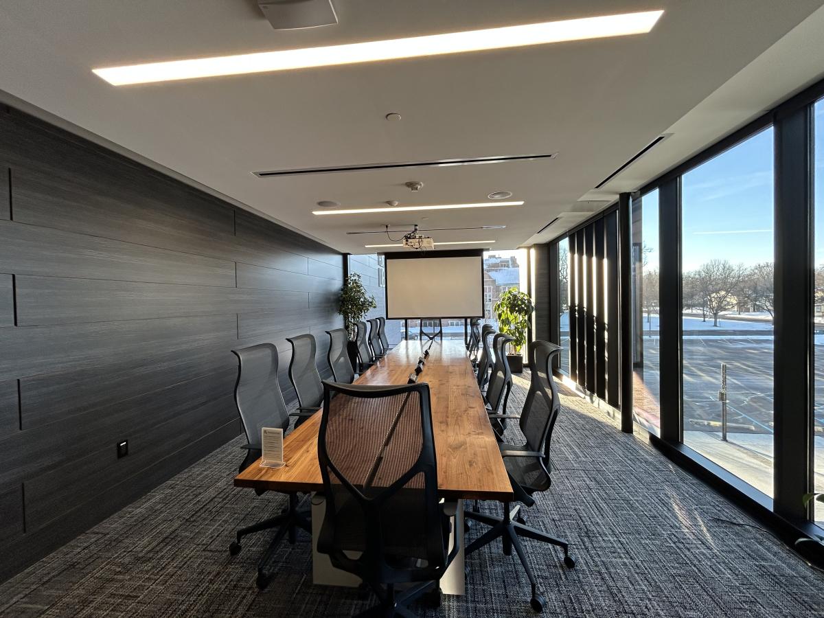 Photo of room with large conference table, 14 chairs and ceiling mounted screen.
