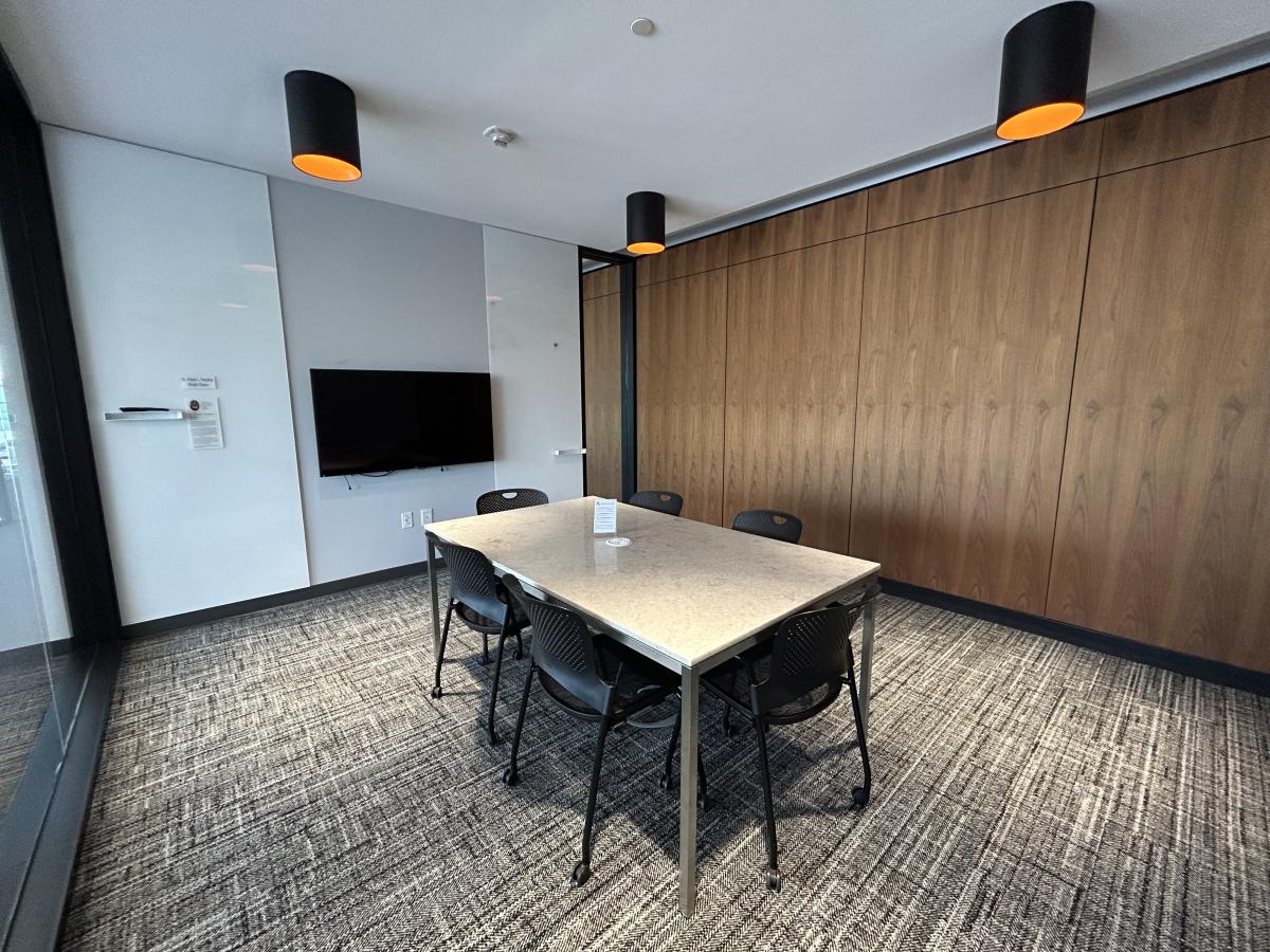 Photo of meeting room with table, six chairs, large monitor on wall and white boards.