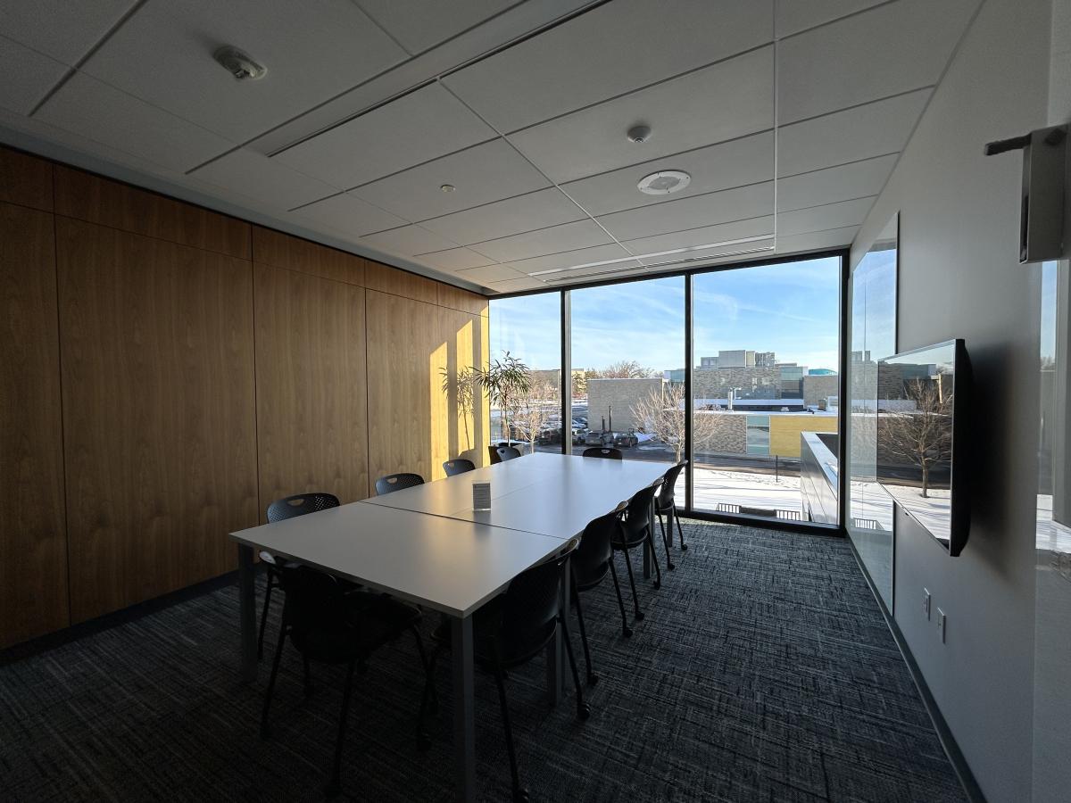 Photo of meeting room with table, ten chairs, large monitor on wall and white boards.