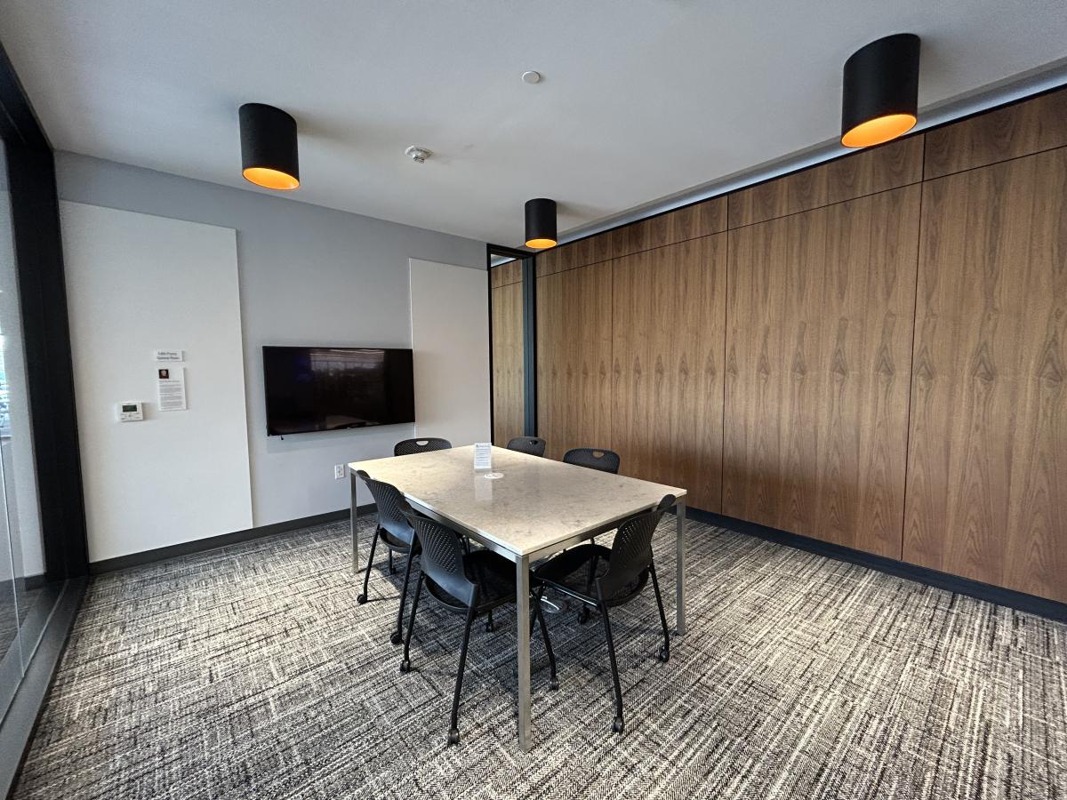 Photo of meeting room with table, six chairs, large monitor on wall and pin boards.