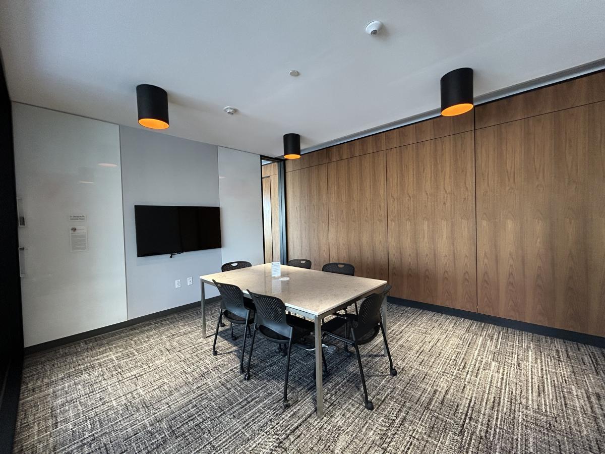 Photo of meeting room with table, six chairs, large monitor on wall and white boards.